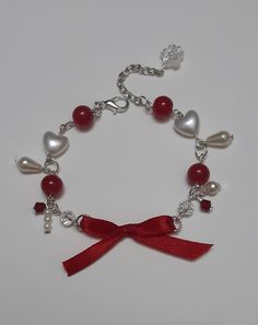 a bracelet with hearts, pearls and red ribbon attached to it on a white surface