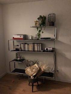 a shelf with books, plants and other things on it in a room that has white walls