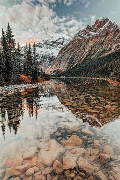 a mountain lake surrounded by trees and rocks in the foreground with a sky filled with clouds