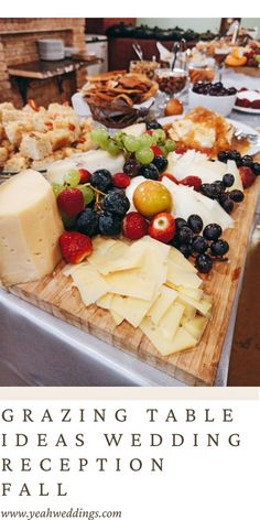 a wooden cutting board topped with lots of cheese and fruit next to other food items