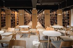 a library filled with lots of wooden tables and chairs next to tall bookshelves