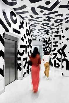 two people are walking through an artisticly designed hallway with black and white letters on the walls