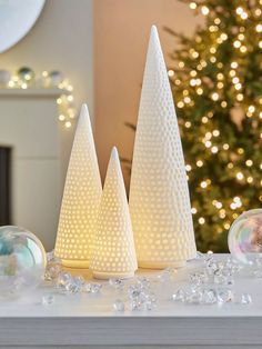 three white christmas trees sitting on top of a table next to a tree with lights