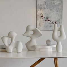 three white vases sitting on top of a table next to a painting and lamp