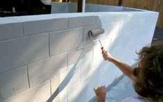 a woman is painting the side of a white brick wall with rollers on it