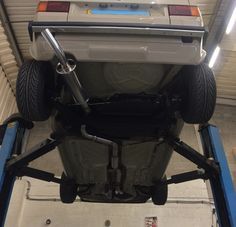 the back end of a white car on a lift in a garage with other vehicles