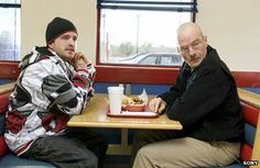 two men sitting at a table with food in front of them and one is eating