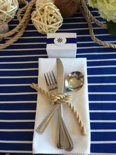 a place setting with silverware and napkins on a blue striped table cloth next to twine rope