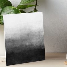 a white and black ombreed card sitting on top of a table next to a potted plant