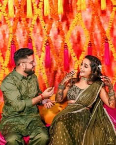 a man and woman sitting next to each other in front of a wall with flowers