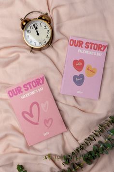 two valentine's day greeting cards next to an alarm clock on a bed with pink sheets