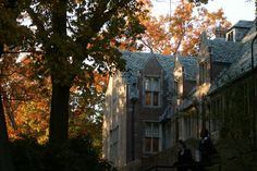 two people are walking up the stairs in front of an old building with fall foliage