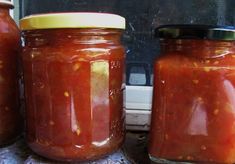 three jars filled with red sauce sitting on top of a counter next to a window