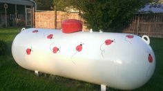 a large white tank with red ladybugs painted on it's side sitting in the grass