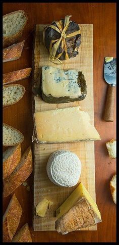 several different types of cheese on wooden cutting boards with bread slices and knifes next to them