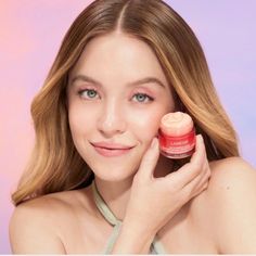 a woman holding up a jar of skin care product in front of her face and looking at the camera