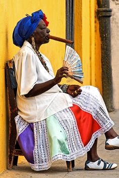 a woman sitting on a bench with a fan in her hand and wearing a colorful dress