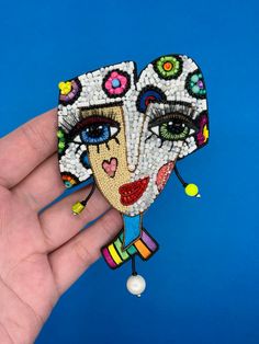 a hand holding up a colorful mask made out of beaded beads on a blue background