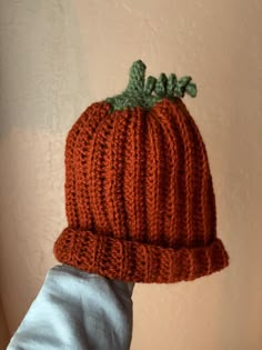 an orange knitted pumpkin hat with green leaves on it's brimmed top