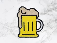 a yellow beer mug embroidered patch on a white marble surface with black and grey lines