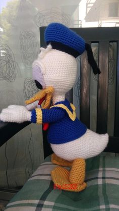 a crocheted stuffed duck wearing a blue and white outfit, holding a tennis racket