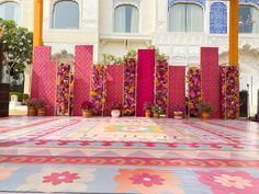 an outdoor area with colorful rugs and potted plants on the ground in front of a building