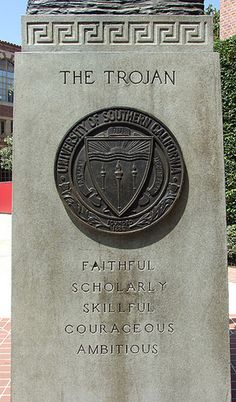 a monument with a shield on it in the middle of a brick walkway next to a building