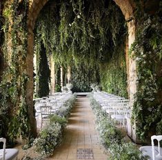 an outdoor ceremony setup with white chairs and greenery on the walls, along with rows of ivy covered archways