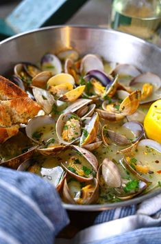 a pan filled with clams and bread on top of a table next to a lemon wedge