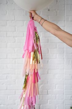 a person holding a white balloon with pink and gold streamers hanging from it's side