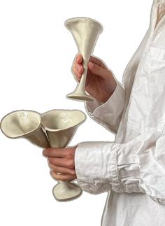 a person holding three white vases in one hand and another with two bowls on the other