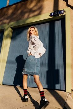 a woman standing in front of a garage door wearing a denim skirt and black socks