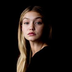 a woman with long blonde hair standing in front of a black background and looking at the camera