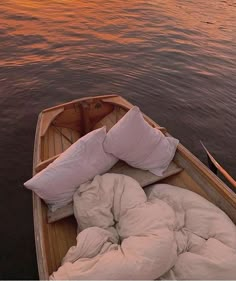 a small boat with pillows and blankets on it in the water at sunset or dawn