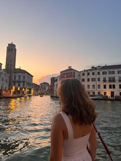 a woman is looking out over the water at buildings and boats in the distance on a canal