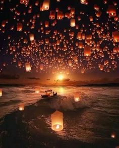 many lanterns floating in the air over water at night with people on a small boat