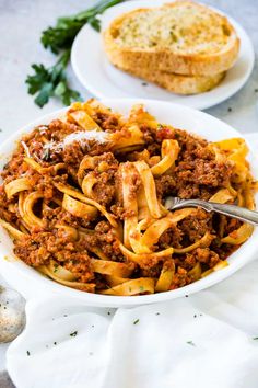 a white bowl filled with pasta and meat on top of a table next to bread