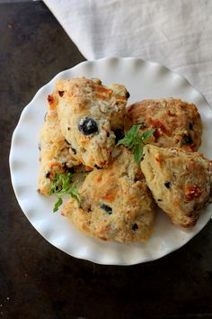 four biscuits on a white plate topped with greens and black olives sitting on a table