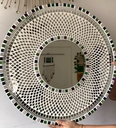 a person holding up a circular mirror that has green and white designs on the side