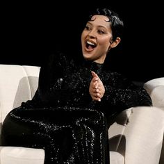 a woman sitting on top of a white chair in front of a black background with her mouth open