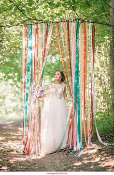 a woman in a wedding dress standing under an arch made out of streamers and ribbons