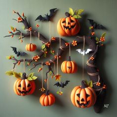 a group of pumpkins hanging from strings with bats and leaves around them on a green wall