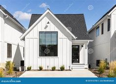 a white house with black shingles and windows in the front yard on a sunny day