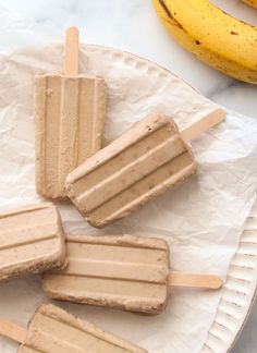 three popsicles on a plate with bananas in the background