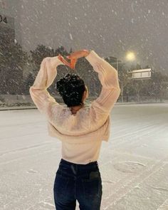 a woman standing in the snow holding her hands up to her head and making a heart shape