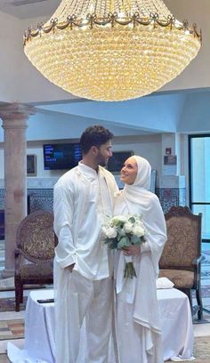 a man and woman standing in front of a chandelier