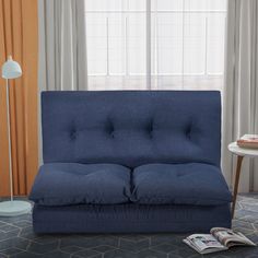 a blue couch sitting in front of a window next to a table with a magazine on it