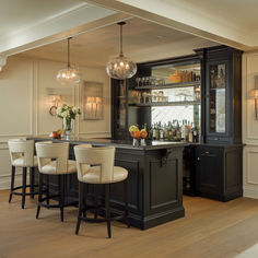 an elegant bar with stools and bottles on the shelves in a room that has wood flooring