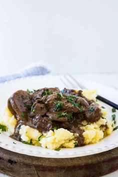 a white plate topped with mashed potatoes and meat covered in gravy next to a fork