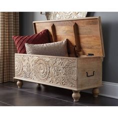 a wooden trunk with decorative carvings on the front and sides, sitting in a living room next to a window